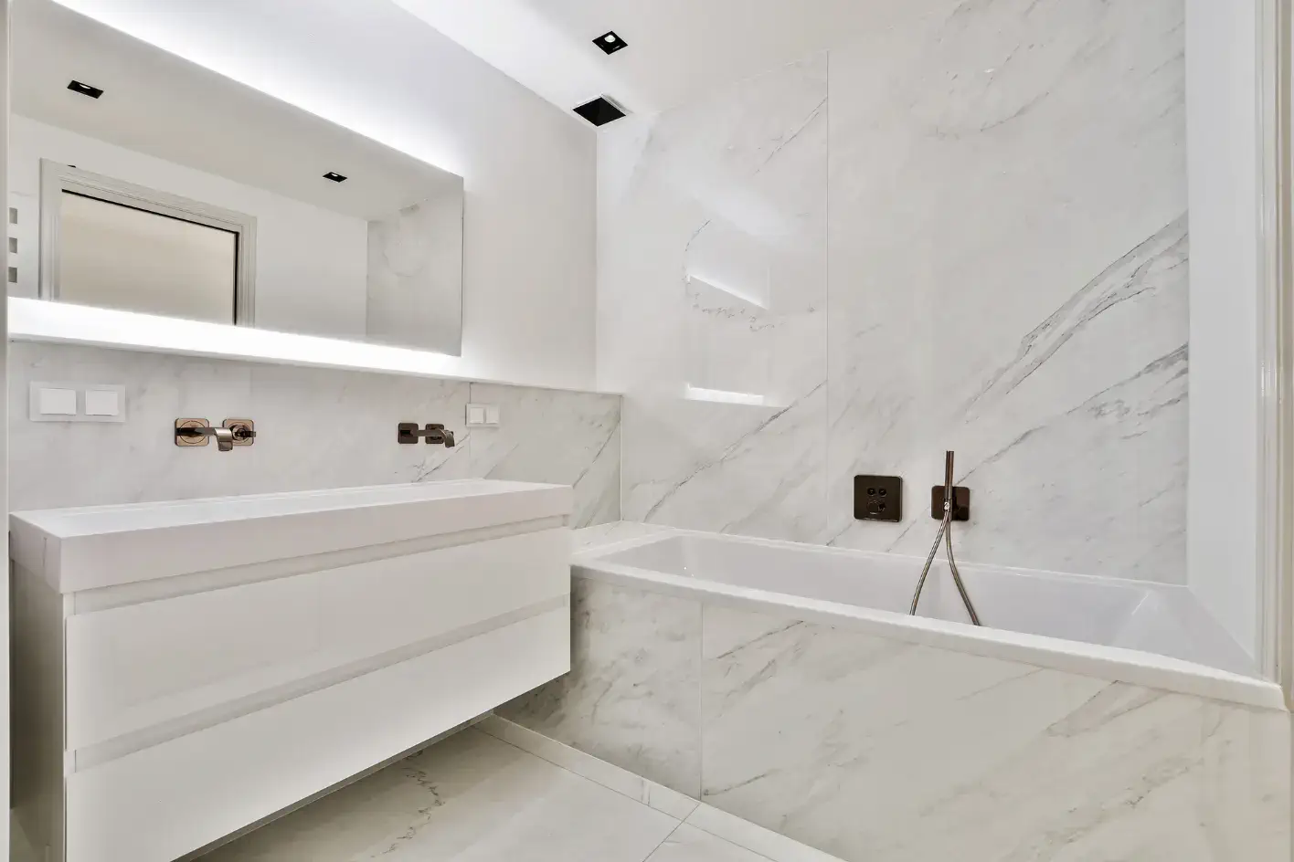 Beyaz mermer kaplama banyo, gömme küvet ve minimalist tasarım.