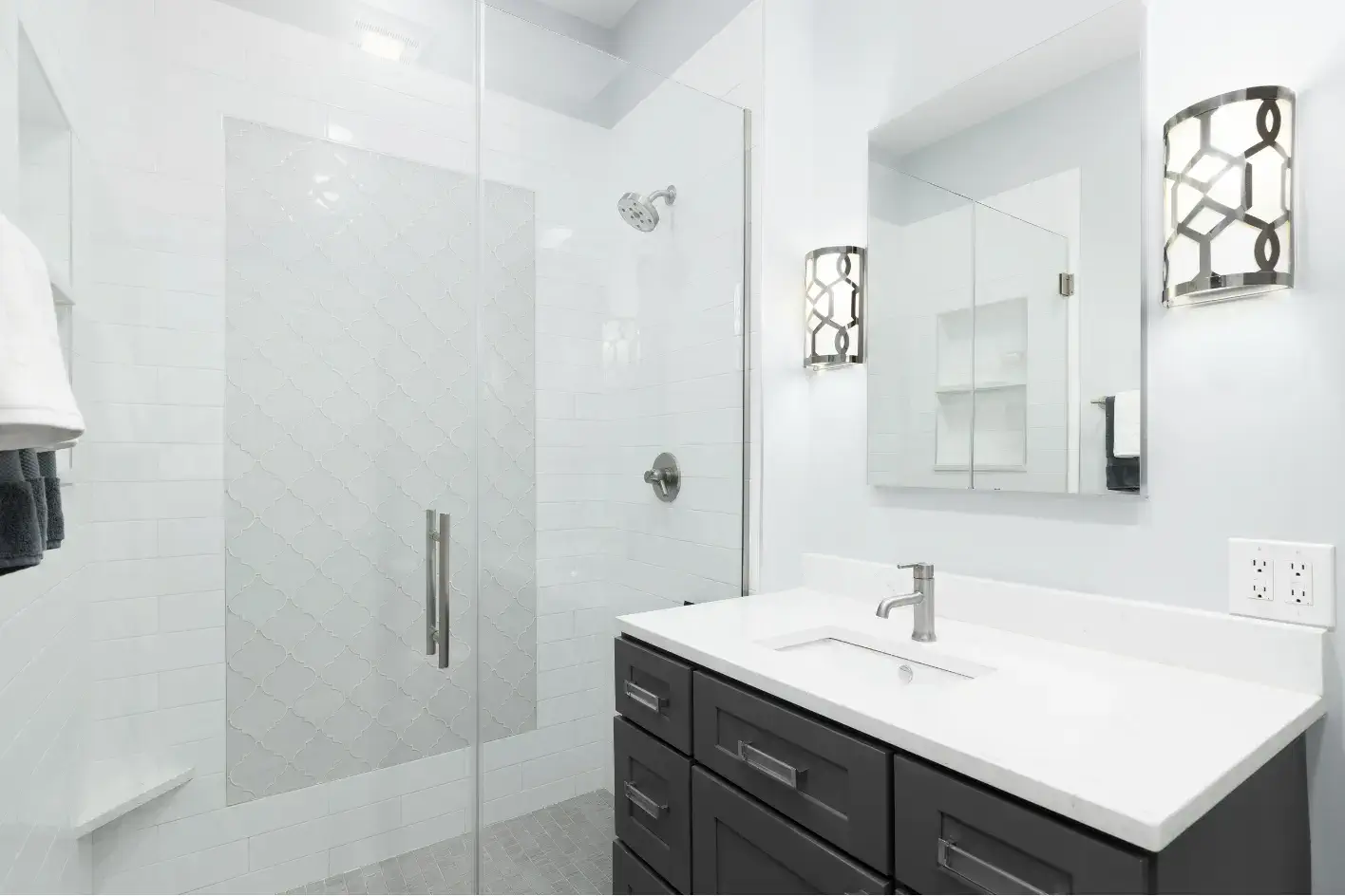 Beyaz metro fayanslı duş ve koyu gri banyo dolabı.