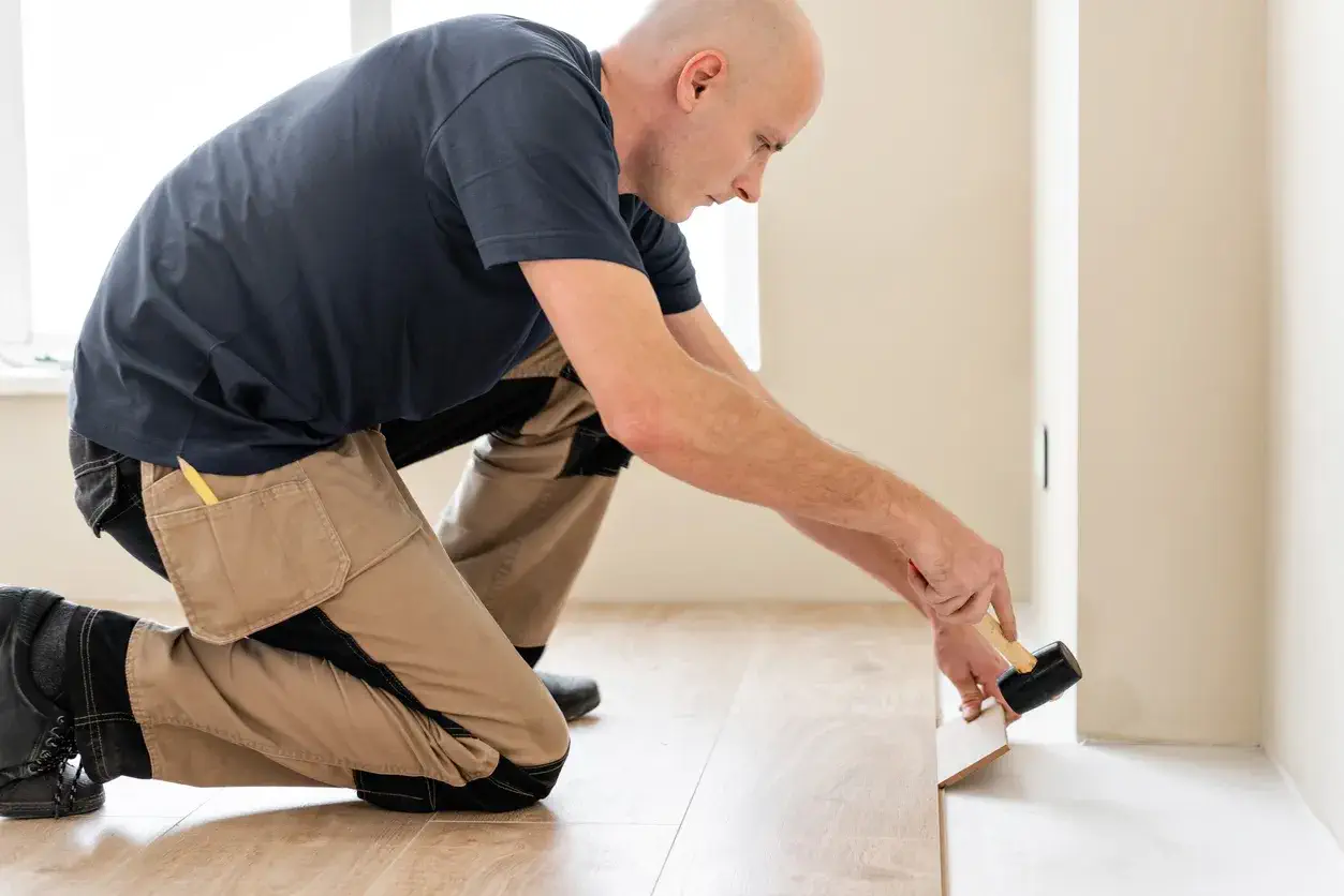 İç mekan zemin yenileme işleminde kauçuk çekiç ile laminat parke döşeyen profesyonel parke ustası